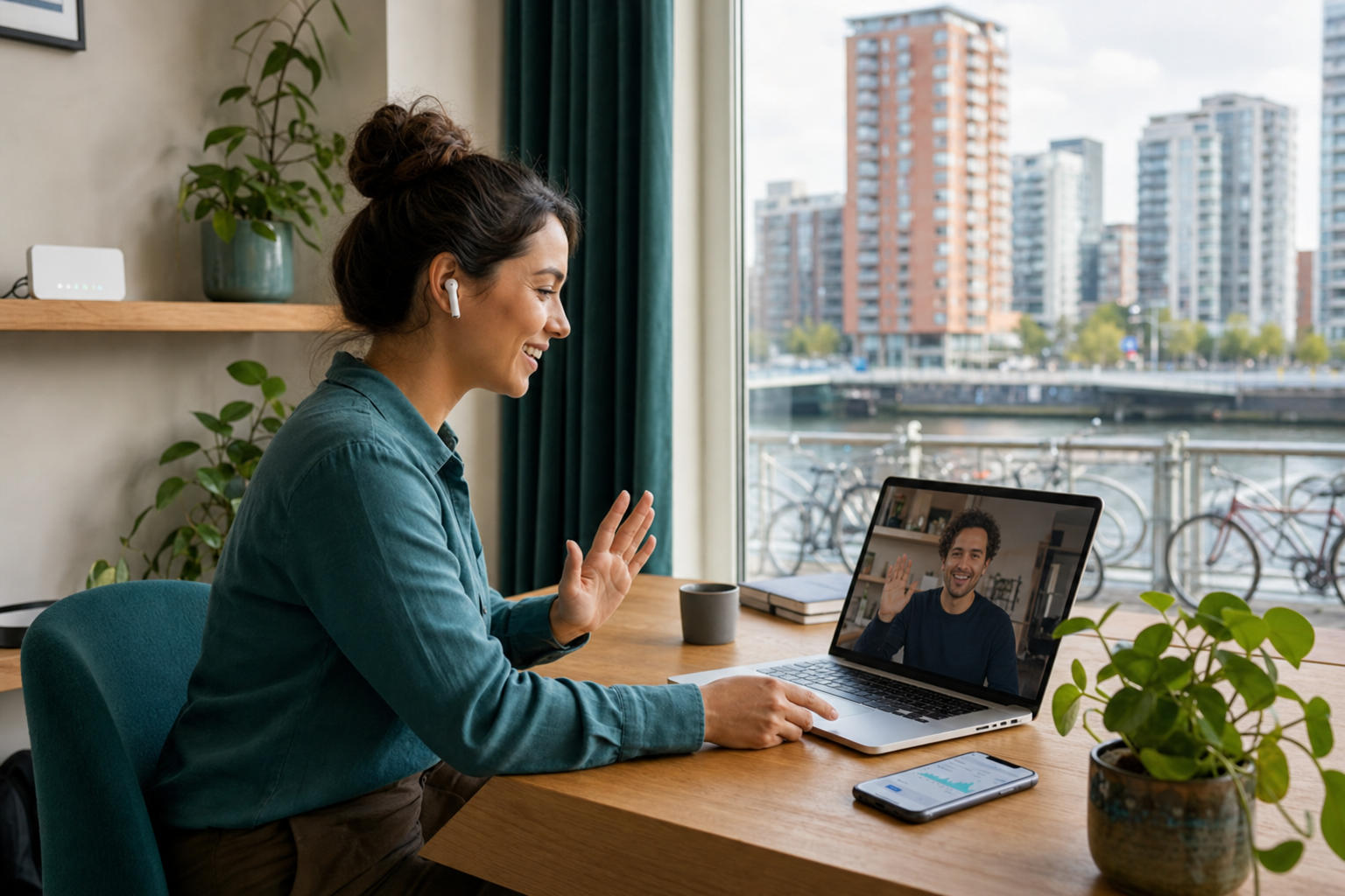 Photorealistic scene of a remote worker in a modern Dutch apartment using a laptop for a video call and a smartphone on the desk, with bicycles and canal buildings visible through the window.